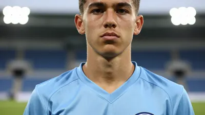Photorealistic close-up of a 16-year-old male Sub-17 football player, lean athletic build, wearing a solid light blue...