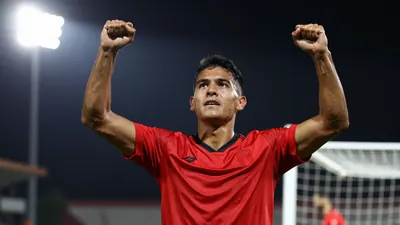 A tight action shot of a Puebla player in a red jersey celebrating a goal, arms raised, face filled with determination