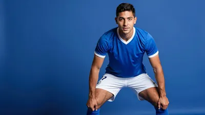 A photorealistic image of a Puebla player, aged 22-25, with a strong build, wearing a blue jersey with white shorts and...