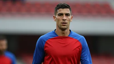 Mid-20s muscular midfielder, face determined, short dark hair, slight stubble, waist-up shot, wearing a plain blue and...