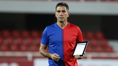 Middle-aged male coach, lean build, waist-up, intense gaze, plain unmarked Puebla training top split blue left, red...