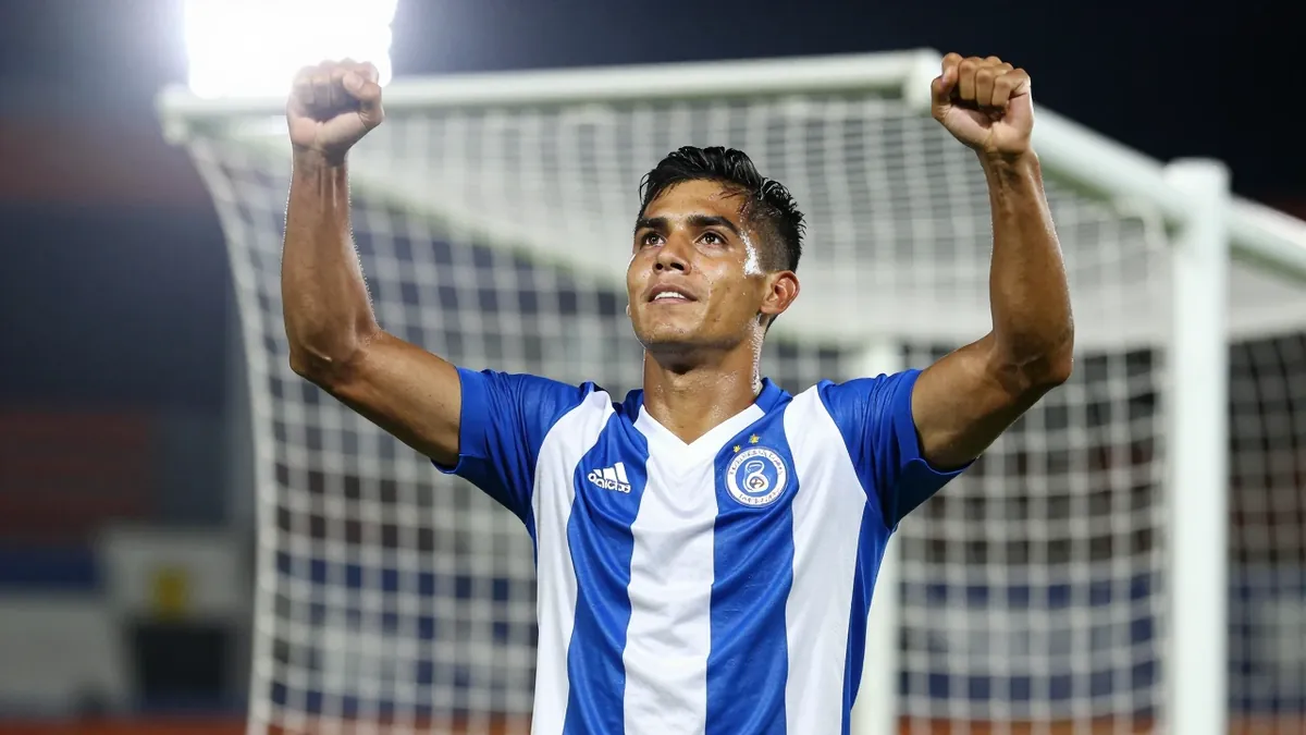 A 30-year-old Puebla player, with a muscular build, wearing a blue and white jersey, celebrating a goal with his arms...